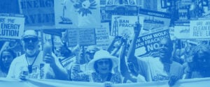 A crowd of protestors stand behind a banner.