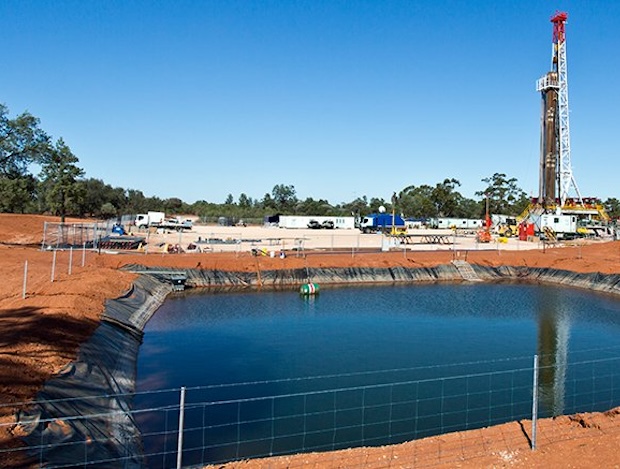 A pool of fracking waste with a wellpad in the background.
