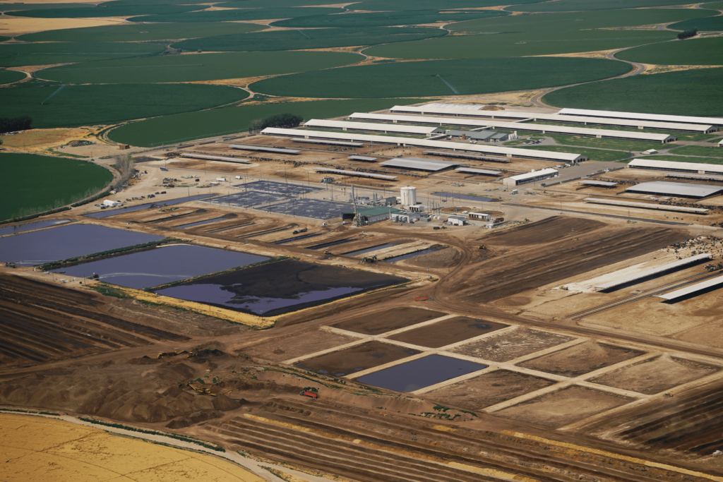 An aerial view of the mega-dairy including long skinny white barns, square manure lagoons, and a white cylinder tower that 