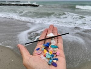 A hand holds a pile of small plastic pieces in front of the waves of an ocean.